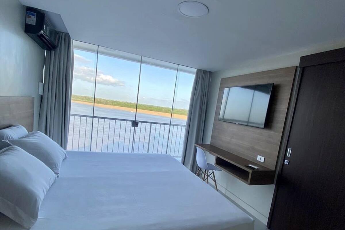A hotel room with a large bed, a TV mounted on the wall, and a view of the water.