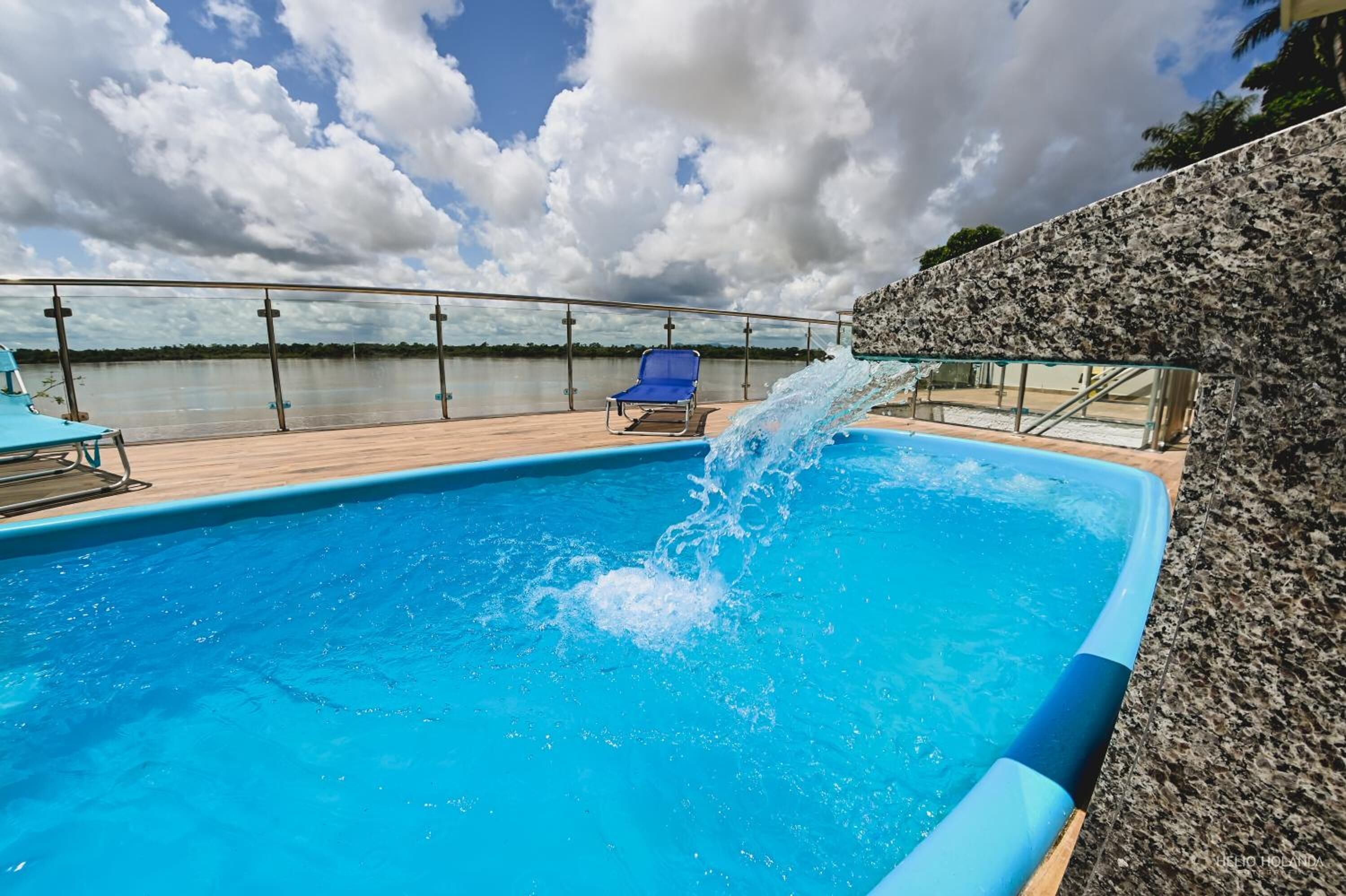 Una piscina con fuente de agua, una silla de descanso azul y vista al cuerpo de agua.
