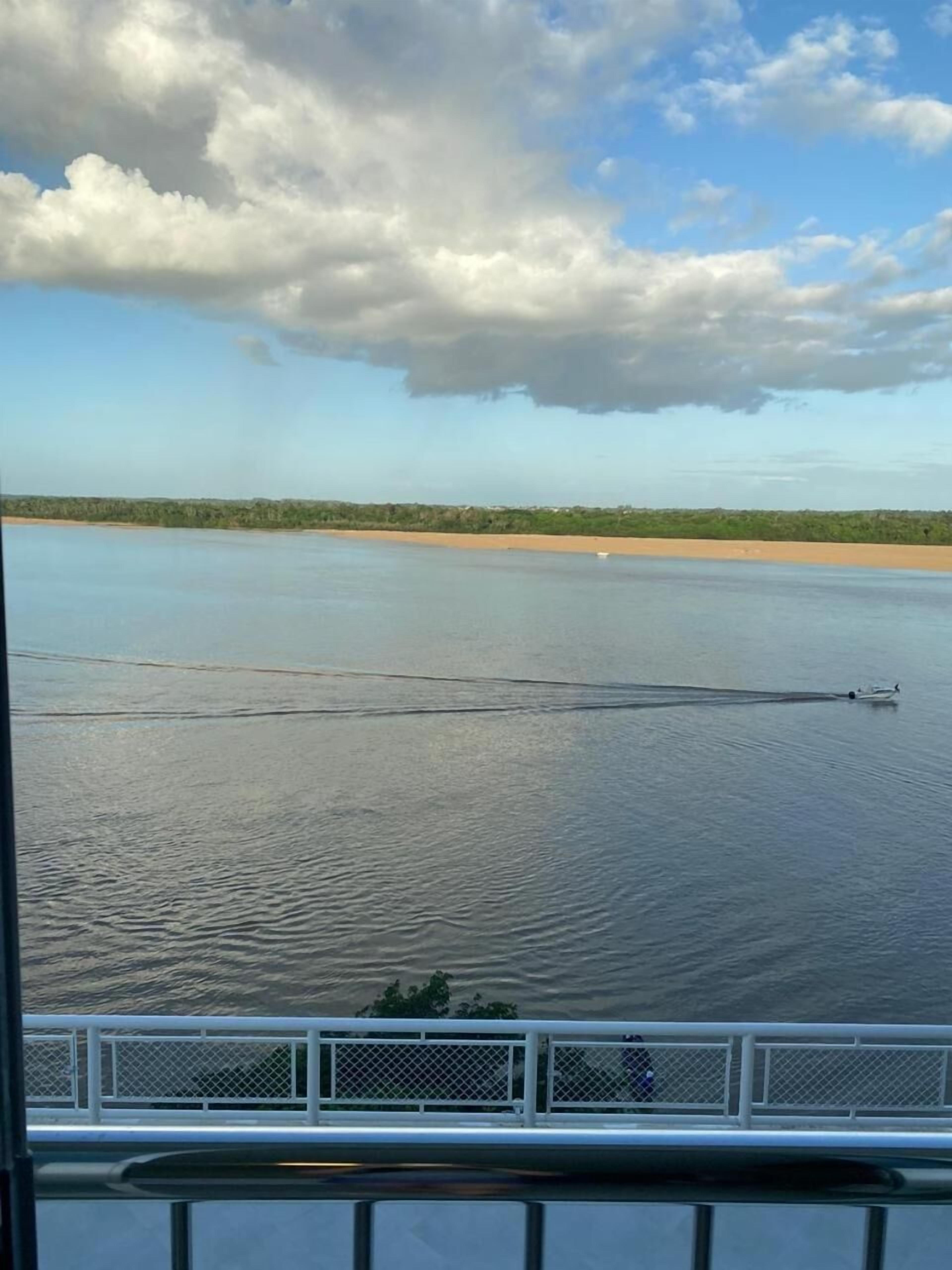 Água calma com uma praia arenosa e uma linha de costa distante.