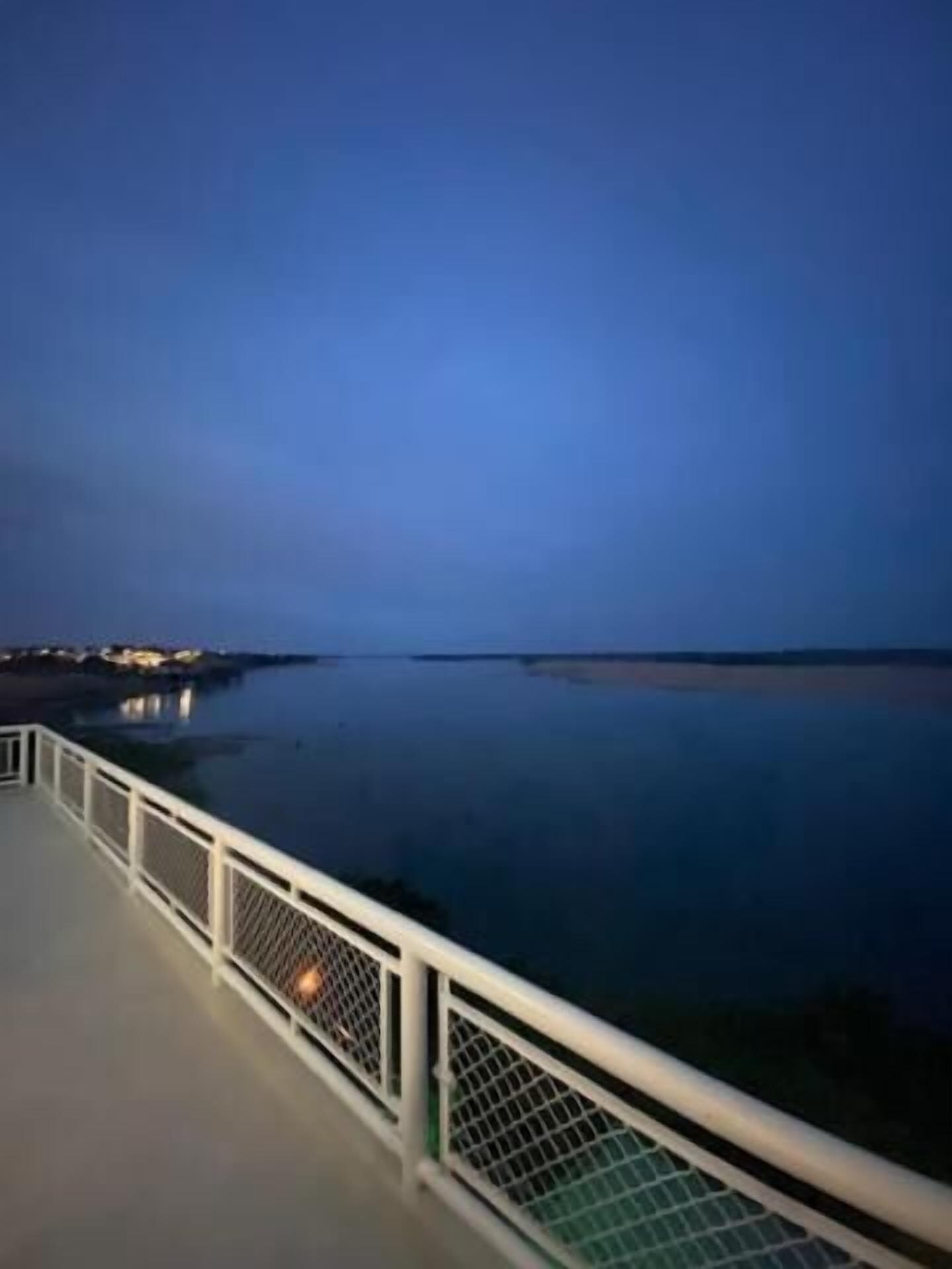 A waterfront promenade with a white railing and calm water.