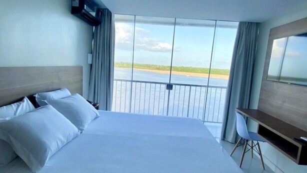 A hotel room with a large bed, a desk, and a view of the beach. - Hotel Orla do Rio Branco (Boa Vista)
