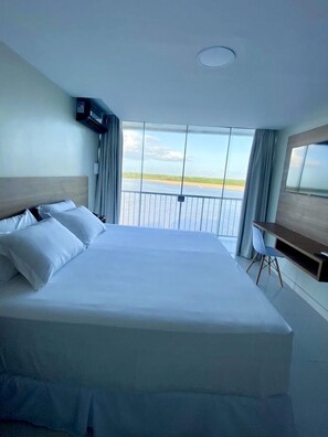 A hotel room with a large bed, a desk, and a view of the beach.