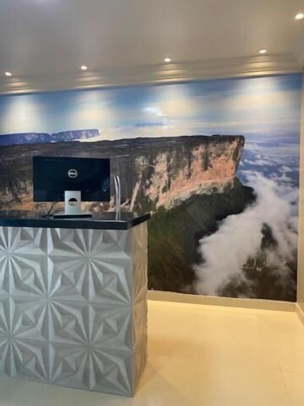A reception desk with a computer monitor, a decorative geometric pattern, and a mural of a mountainous landscape with clouds.