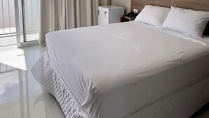 A hotel room with a large bed, a nightstand, a lamp, and a view of the outdoors through a sliding door. - Hotel Orla do Rio Branco (Boa Vista)