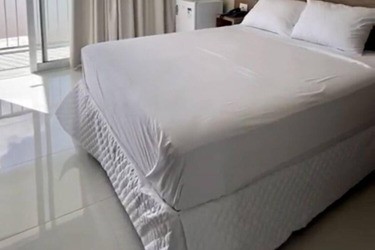 A hotel room with a large bed, a nightstand, a lamp, and a view of the outdoors through a sliding door.