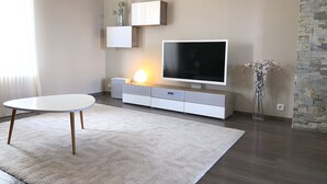 A modern living room with a flat-screen TV, a white console table, a round white table, and a stone accent wall. - Heart of Metz, 2 rooms free parking wifi 75m² "Le Saint Bernard (Metz)