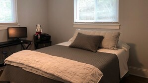 Un dormitorio con cama, escritorio con ordenador y dos ventanas con persianas.