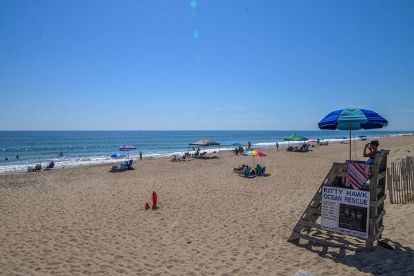 Una playa con sombrillas, sillas de playa y un puesto de salvavidas.