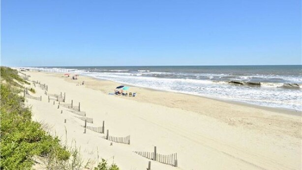 A beach with a wooden fence, a few people, and a beach umbrella. - Sea Scape - Multiple Pools, Amenities, and Close to Beach! (Kitty Hawk)