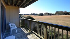 A wooden deck with a railing, a white plastic chair, and a view of a grassy field with trees. - Sea Scape - Multiple Pools, Amenities, and Close to Beach! (Kitty Hawk)