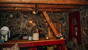 A rustic cabin interior with a loft bed, a wooden dining table, a stone wall, and a cozy seating area. - The Stone Cabin; Off-the-grid experience with outhouse (Houston)