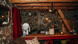 A rustic cabin interior with a wooden dining table, a stone wall, a leather sofa, and a red stool. - The Stone Cabin; Off-the-grid experience with outhouse (Houston)