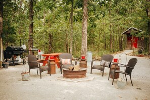 A campsite with a fire pit, chairs, a table, and a grill. - The Stone Cabin; Off-the-grid experience with outhouse (Houston)