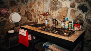 A kitchen with a stone wall, a gas stove, and various kitchen items. - The Stone Cabin; Off-the-grid experience with outhouse (Houston)