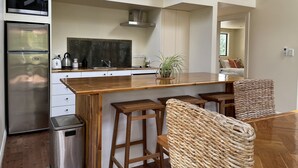 A modern kitchen with a wooden countertop, stainless steel appliances, and a bar area with woven stools. - Moana Apartment with Bush Views and near Surf (Raglan)