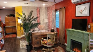 A cozy room with a wooden desk, a comfortable chair, a fireplace, and a television. - Garden-front studio  (Phoenix)