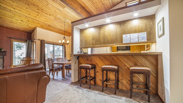 A cozy interior with a wooden ceiling, a brown leather sofa, and a bar area with stools. - Bright Cozy Snowcreek 1Bed/1Bath WIFI (Mammoth Lakes)