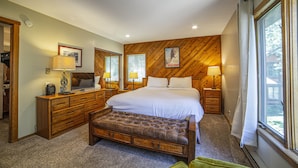 A bedroom with a large bed, wooden headboard, two bedside tables with lamps, a bench, and a window with curtains. - Bright Cozy Snowcreek 1Bed/1Bath WIFI (Mammoth Lakes)