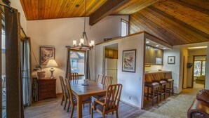 A spacious dining area with a wooden table and chairs, a chandelier, and a view of the kitchen and living area through an open doorway. - Bright Cozy Snowcreek 1Bed/1Bath WIFI (Mammoth Lakes)