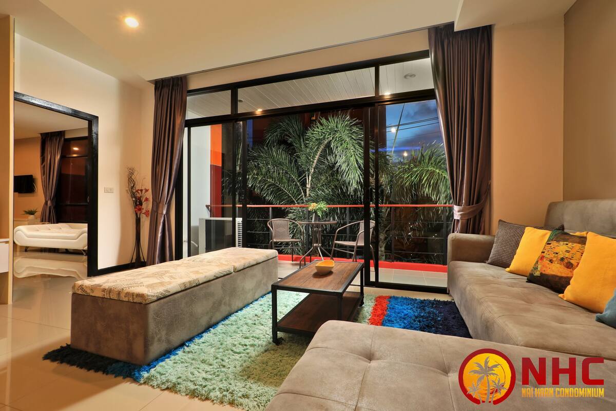 A modern living room with a sofa, a bench, a coffee table, and a view of a balcony with plants and a railing.