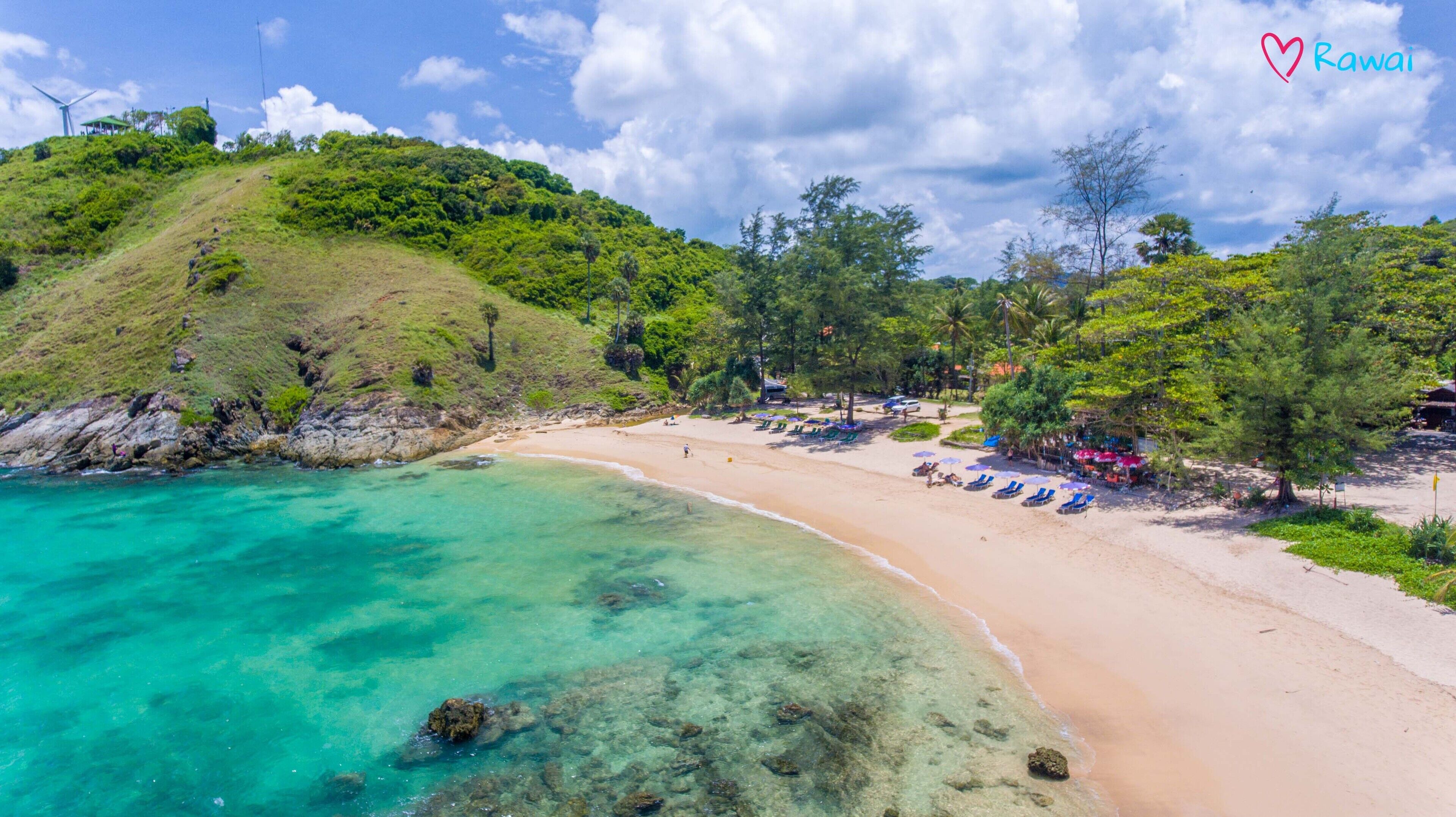Una playa con aguas turquesas cristalinas, una orilla de arena y una loma verde exuberante.