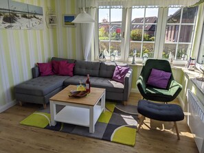 A living room with a grey sectional sofa, a green armchair, a wooden coffee table, and a view of the outside through large windows.