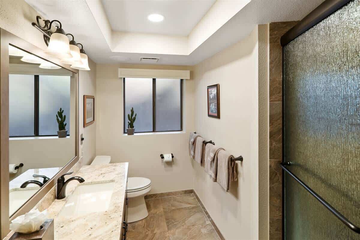 Une salle de bain avec un lavabo en marbre, des toilettes, une douche avec une porte en verre et une fenêtre donnant sur un beau paysage.