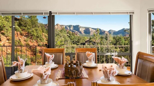 Une table à manger avec des chaises, une pièce décorative en guise de centre de table, et une vue sur les montagnes par de grandes fenêtres.