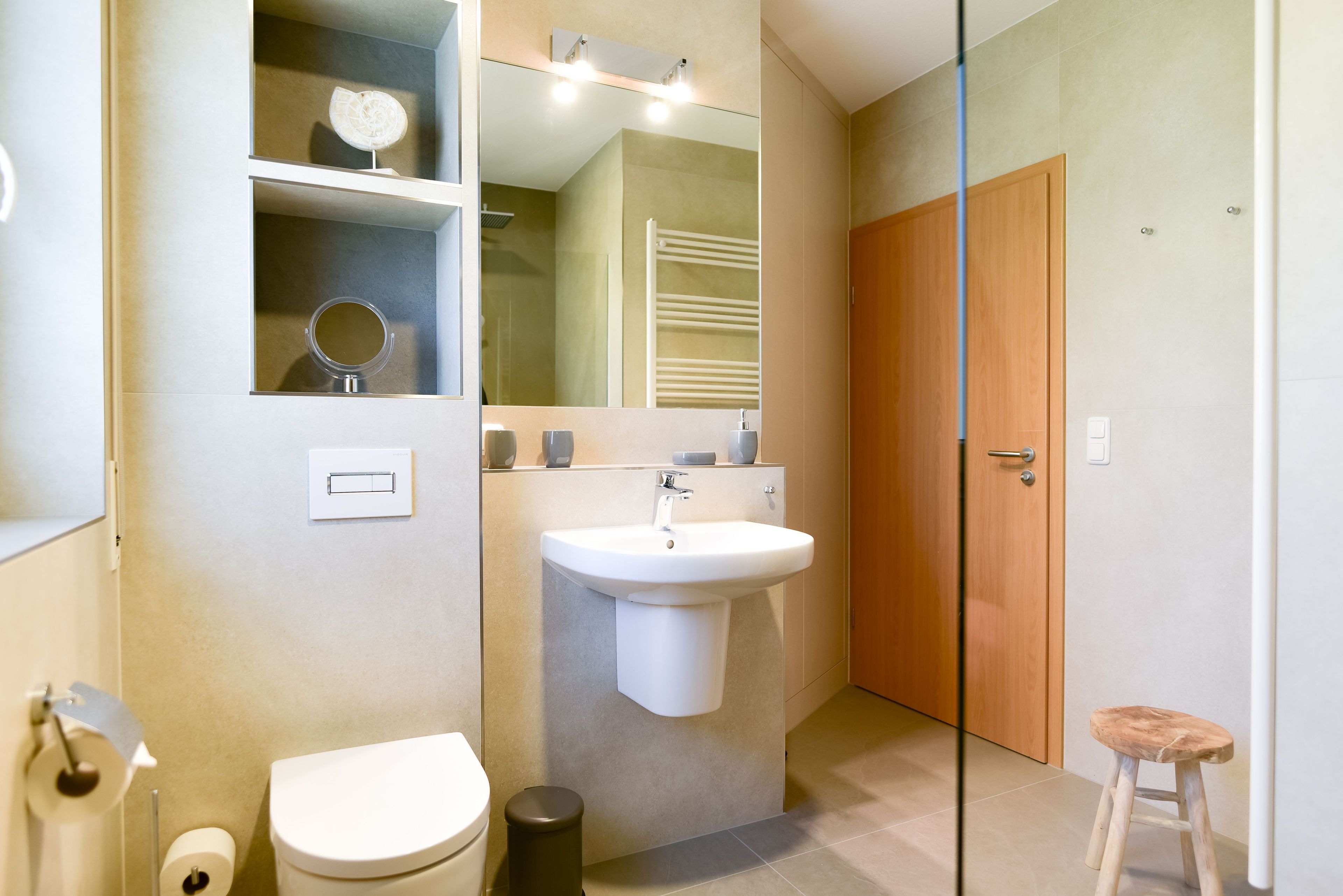 Ein Badezimmer mit Toilette, Waschbecken, Spiegel und einer Holztür.