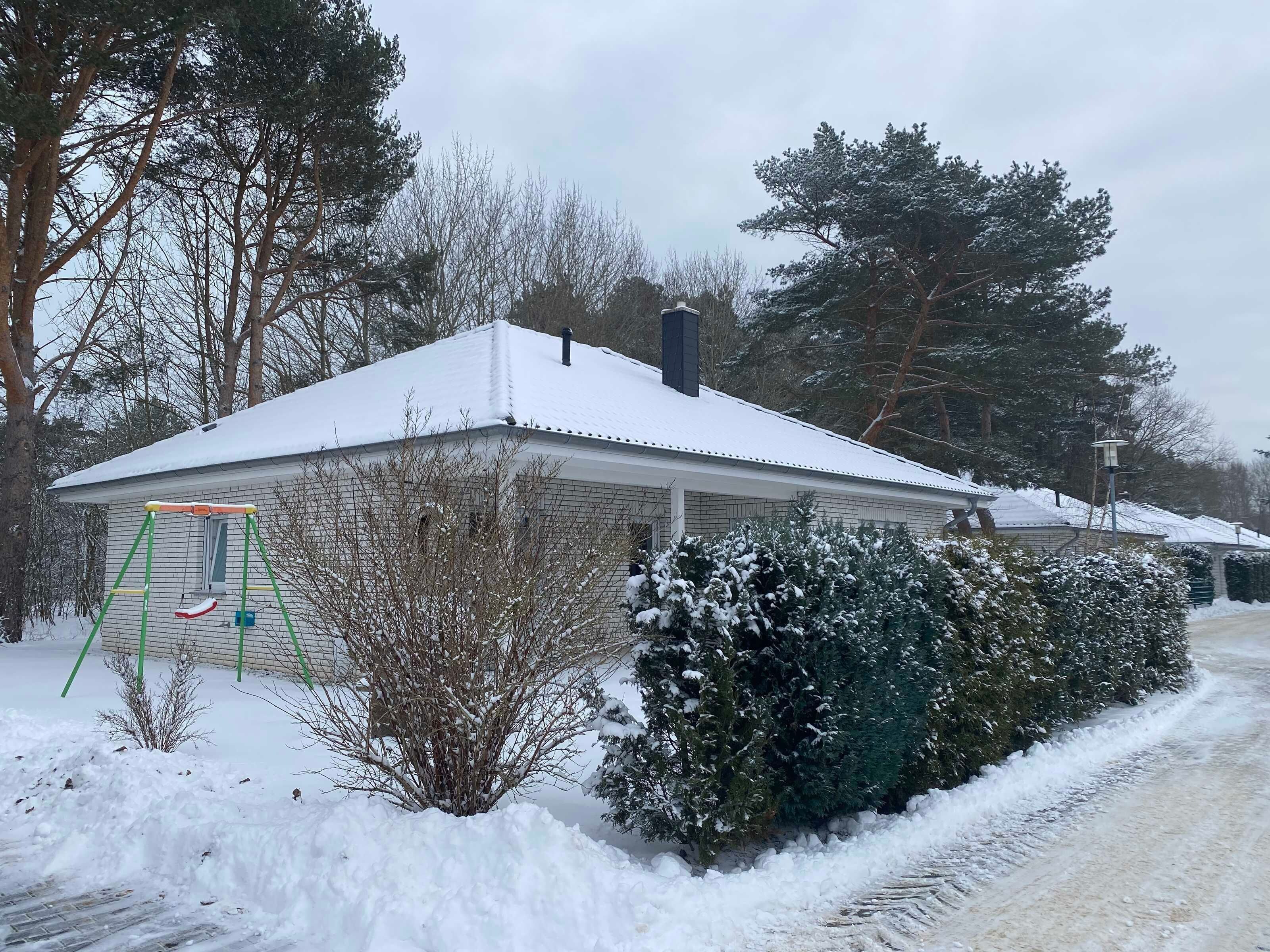 Una casa cubierta de nieve con una chimenea visible, un aro de baloncesto y una entrada cubierta de nieve.