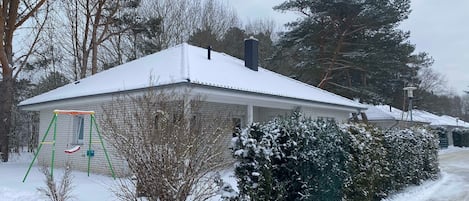 Una casa cubierta de nieve con una chimenea visible, un aro de baloncesto y una entrada cubierta de nieve.