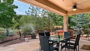 Eine Terrasse im Freien mit einem Tisch und Stühlen aus Glas, umgeben von Pflanzen und einem Steinboden.