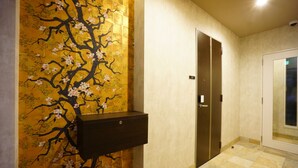 A hallway with a wall mural of a tree with flowers, a door, and a small cabinet. - Rona Hotel (Tokyo)