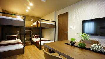 A room with bunk beds, a wooden table, a television, and a small potted plant.