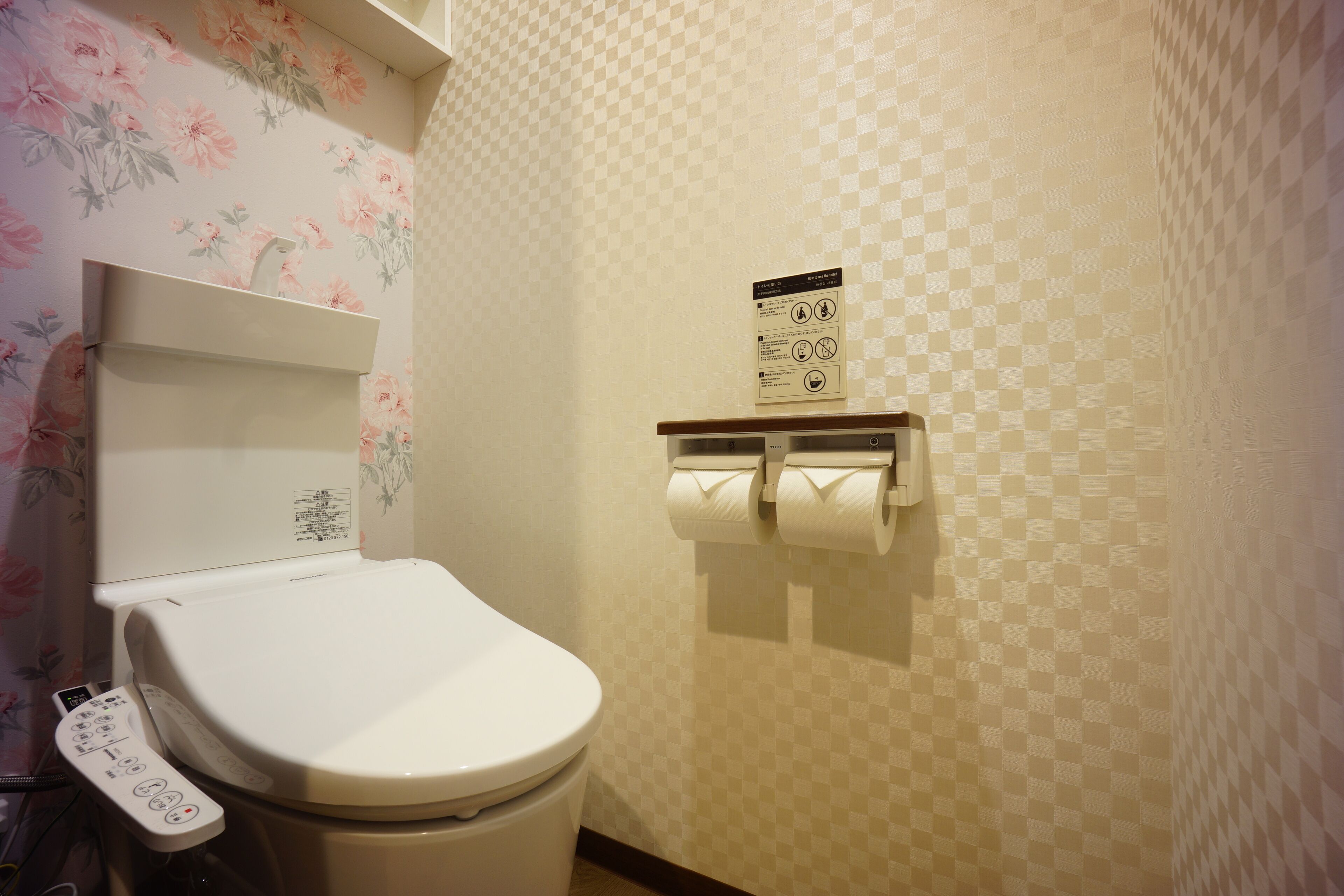 A bathroom with a toilet, a toilet paper holder, and a wall-mounted sign with instructions.