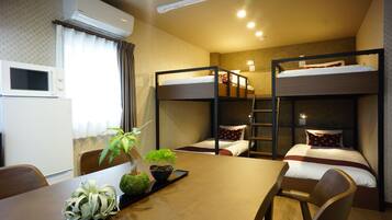 A hotel room with bunk beds, a dining table with chairs, a microwave, and a potted plant.
