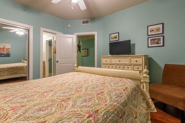 A bedroom with a bed, dresser, TV, and framed pictures on the wall. - Charming Poolside Condo with Bay Views! Complimentary Boat Slip! (Orange Beach)