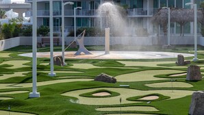 Un jardin aménagé avec une fontaine, des colonnes blanches et un bâtiment doté de balcons en arrière-plan.