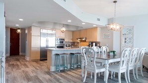 A modern kitchen with a central island, bar stools, and white chairs. - Timeless Three Bedroom Condo with Stunning Gulf Views! Complimentary Boat Slip! (Orange Beach)