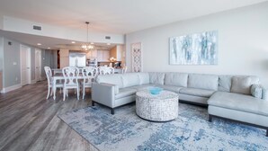 A modern living room with a sectional sofa, a round coffee table, and a dining area with white chairs. - Timeless Three Bedroom Condo with Stunning Gulf Views! Complimentary Boat Slip! (Orange Beach)