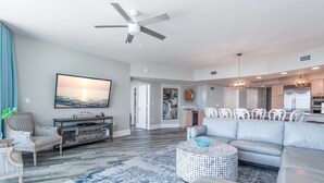 A spacious living room with a large gray sectional sofa, a round coffee table, and a television mounted on the wall. - Timeless Three Bedroom Condo with Stunning Gulf Views! Complimentary Boat Slip! (Orange Beach)