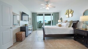 A bedroom with a bed, a ceiling fan, a dresser, a nightstand, a lamp, a mirror, and a view of the outdoors. - Beautifully Decorated Three Bedroom/Three Bath Condo Sleeping 10. Complimentary Boat Slip! (Orange Beach)