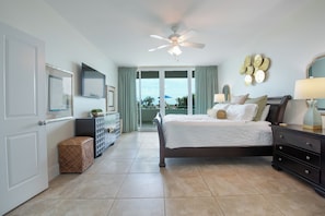 A bedroom with a bed, a ceiling fan, a dresser, a nightstand, a lamp, a mirror, and a view of the outdoors.