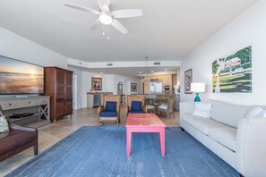 A spacious living room with a ceiling fan, a large flat-screen TV, a wooden cabinet, and a dining area with wicker chairs and a table.