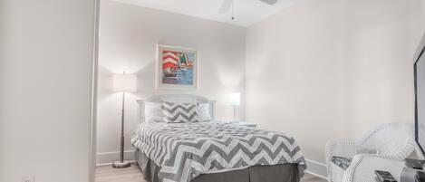 A bedroom with a bed, a standing lamp, a ceiling fan, and a wicker chair.