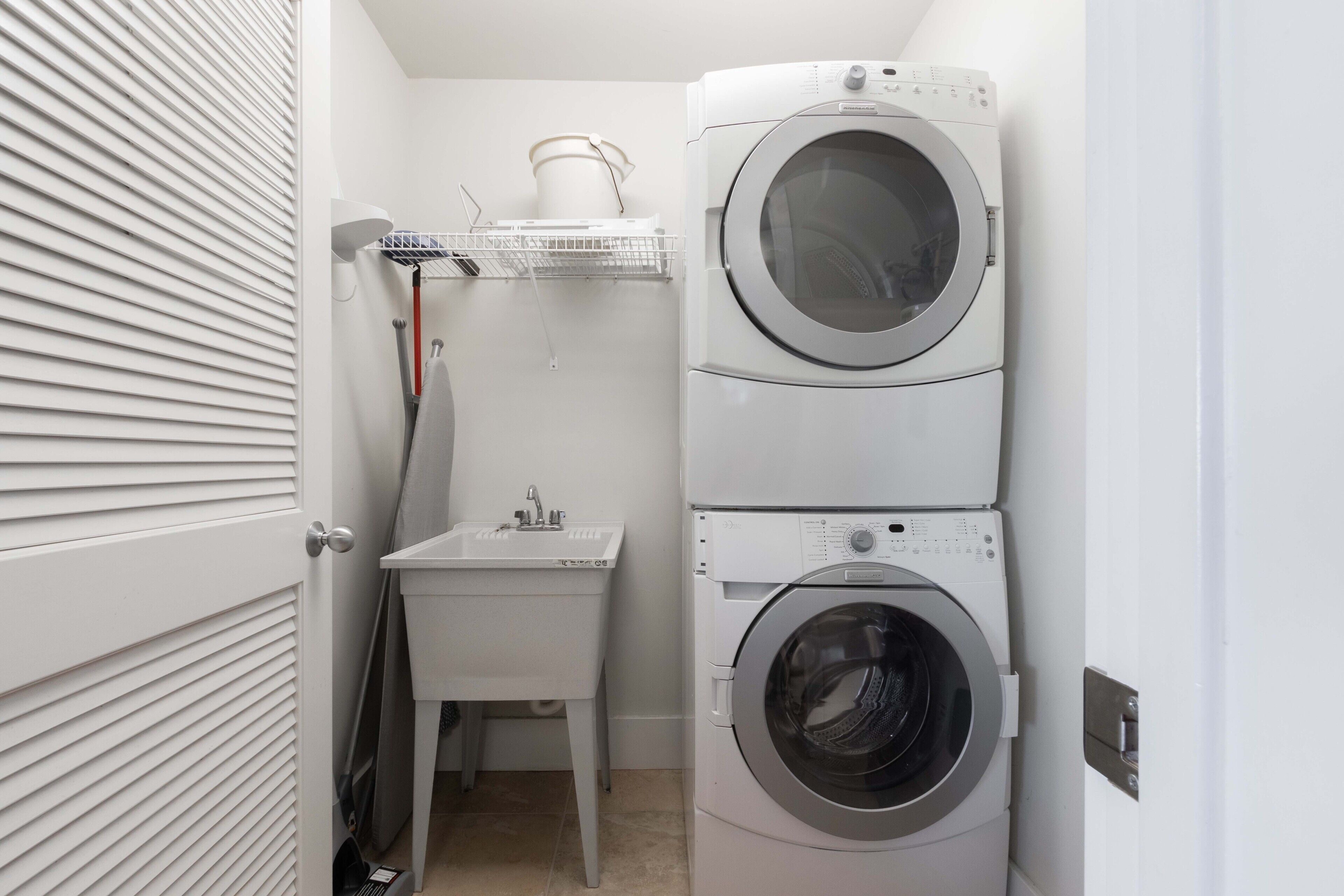 Une petite buanderie comprenant une machine à laver et un sèche-linge superposés, un petit évier et un étendoir.