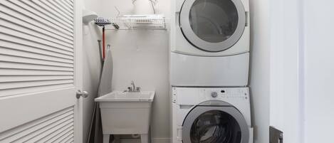 Une petite buanderie comprenant une machine à laver et un sèche-linge superposés, un petit évier et un étendoir.