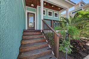 Stunning home with a wooden staircase and lush greenery surrounding the entrance.