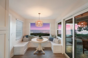 A cozy seating area with a view of the ocean at sunset, featuring a round table and cushioned benches. - Ship Watch: Private Beach, North End, Dog Friendly by Anna Maria Life Vacation Rentals (Anna Maria)