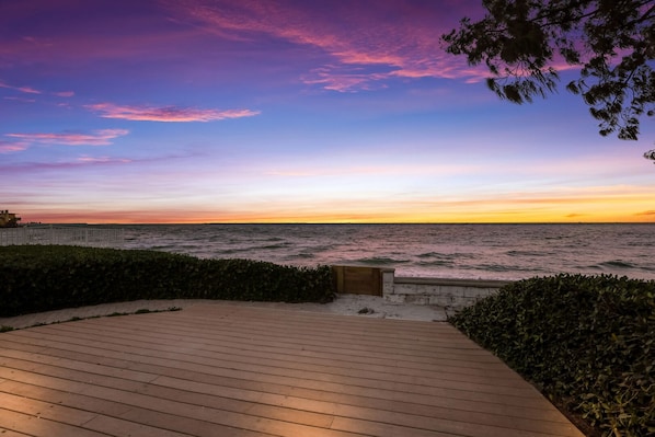 A wooden deck with a view of the ocean at sunset. - Ship Watch: Private Beach, North End, Dog Friendly by Anna Maria Life Vacation Rentals (Anna Maria)